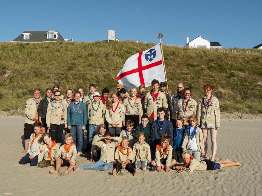 Gruppenfoto aus dem SoLa 2023, die mitgefahrenen Pfadfinder*innen sammeln sich am Strand. Hinter ihnen weht das Banner der DPSG