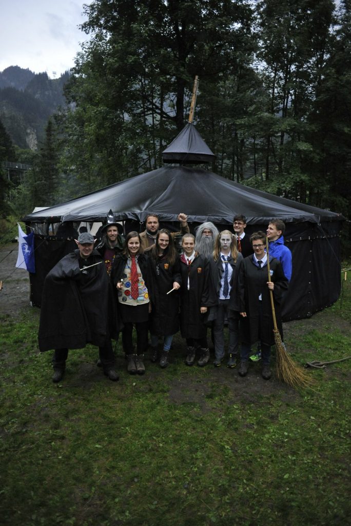 Ein Teil der Leitungsrunde im SoLa 2018. Leitende stehen im Grünen vor einer nassen Jurte. Sie sind dem Motto des SoLas nach in Harry Potter Kostümen verkleidet.